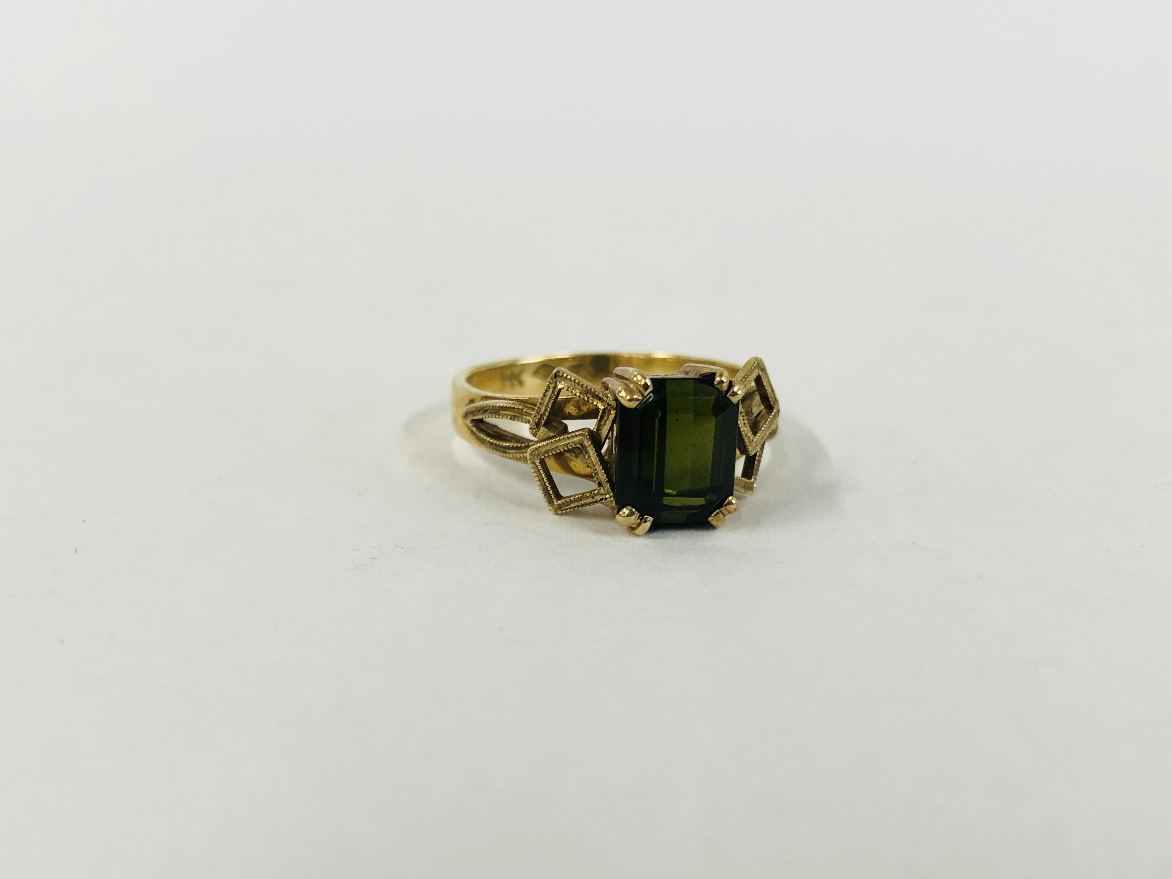 AN UNUSUAL 9CT GOLD RING, CENTRAL EMERALD CUT GREEN STONE SURMOUNTED BY OVERLAYED SQUARES.