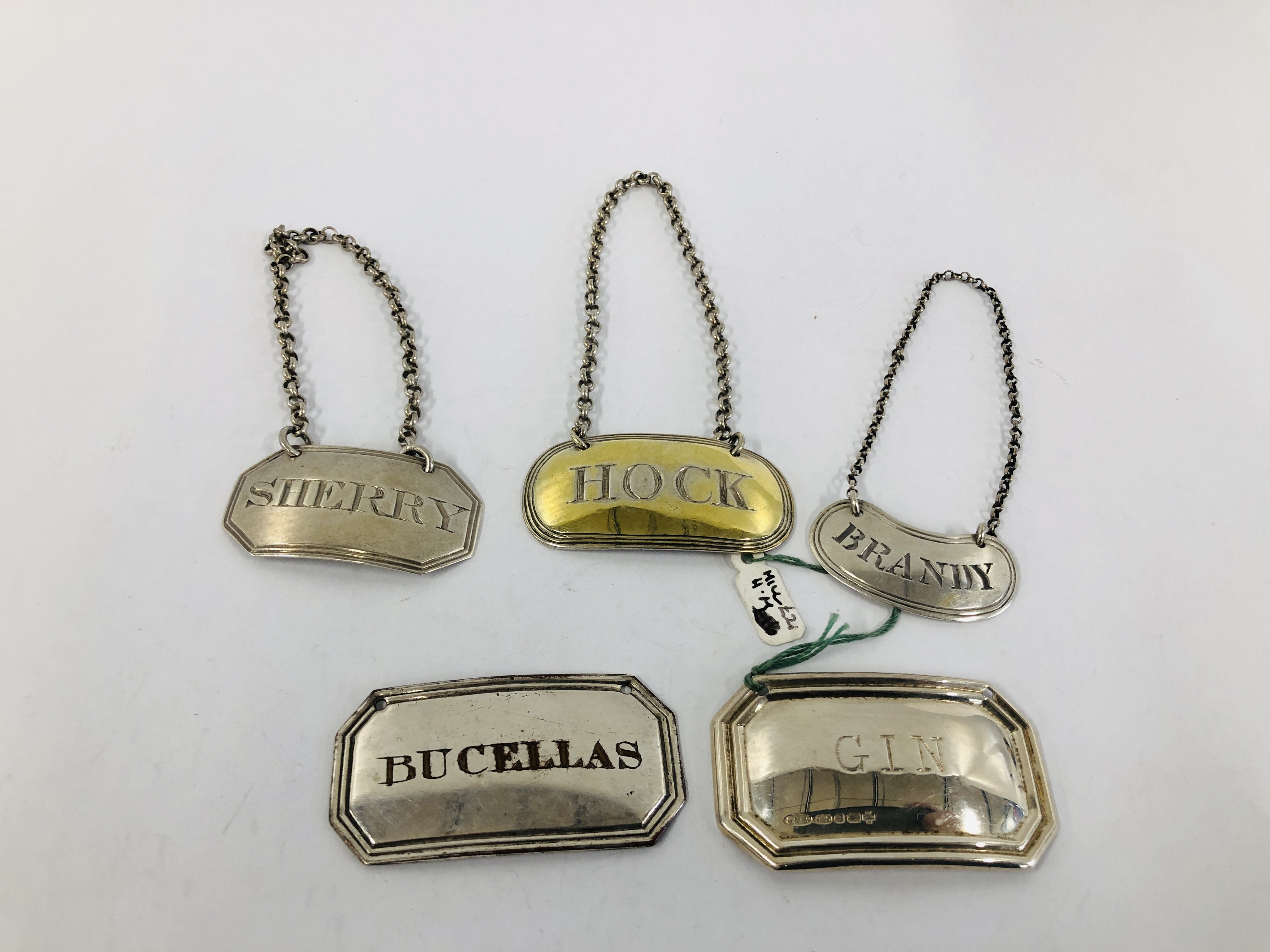 A GROUP OF FOUR SILVER WINE LABELS, BRANDY, HOCK, GIN AND SHERRY ALONG WITH A PLATED EXAMPLE,