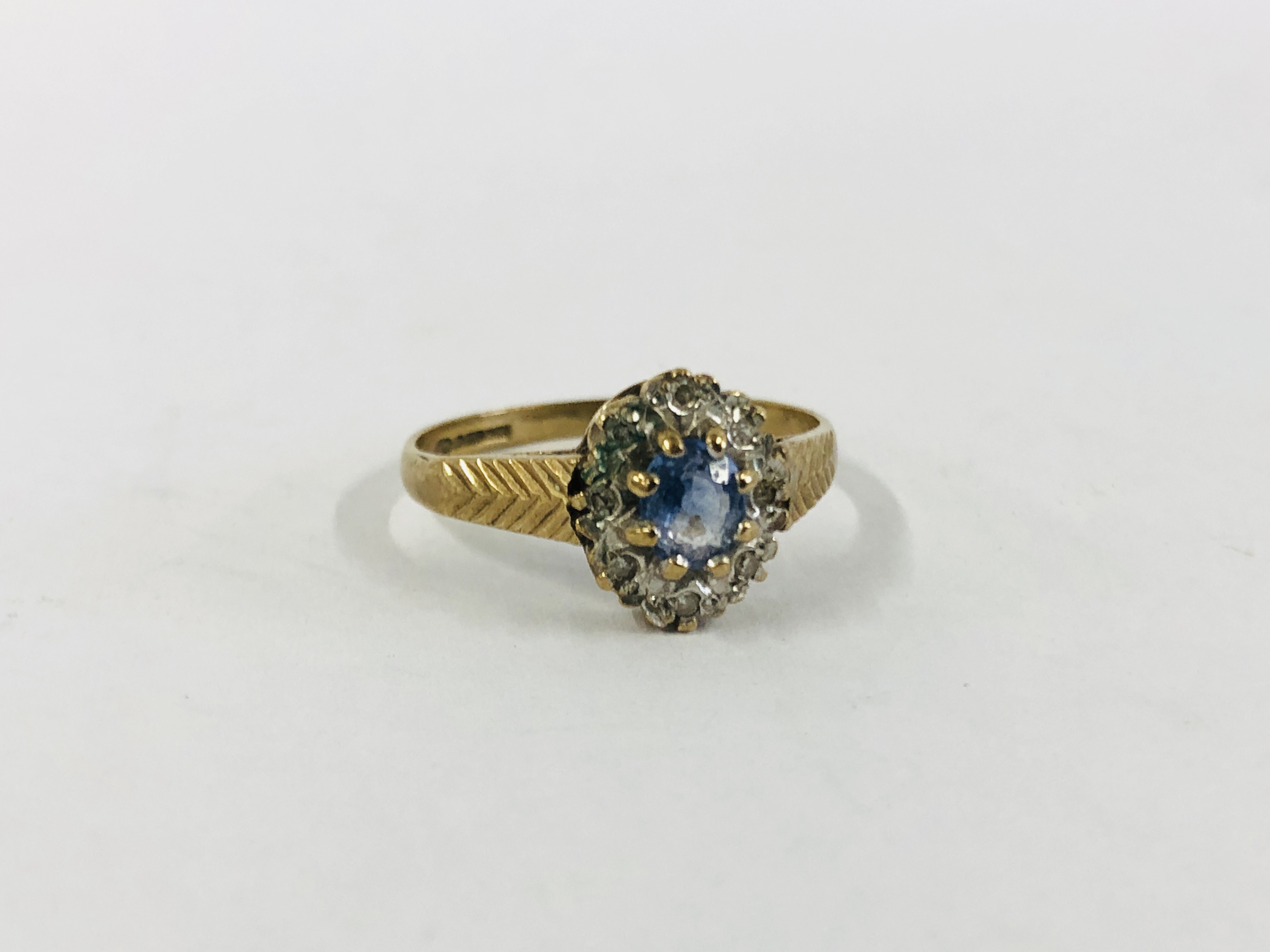 AN ATTRACTIVE 9CT GOLD DRESS RING SET WITH CENTRAL PALE BLUE STONE, SURROUNDED BY SMALLER DIAMONDS.