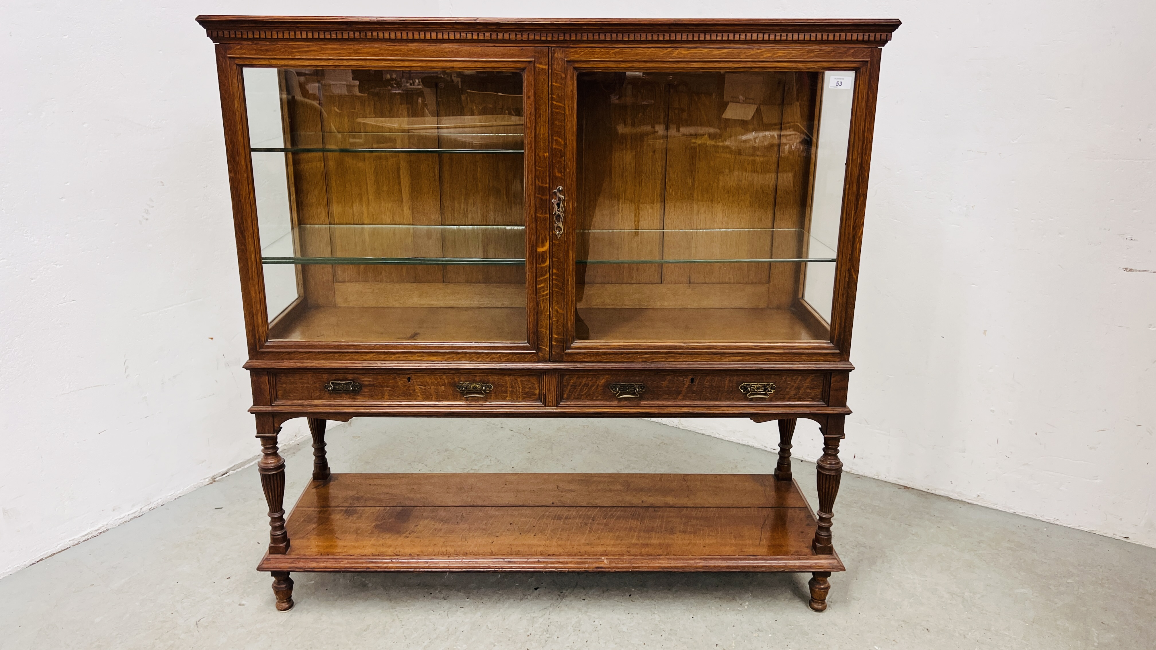 AN EDWARDIAN OAK GLAZED DISPLAY CABINET ABOVE A TWO DRAWER AND OPEN SHELF BASE WIDTH 122CM.