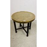 A CIRCULAR BRASS TOP OCCASIONAL TABLE WITH IRANIAN DESIGN ON FOLDING OAK BASE DIA. 59CM.