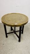 A CIRCULAR BRASS TOP OCCASIONAL TABLE WITH IRANIAN DESIGN ON FOLDING OAK BASE DIA. 59CM.