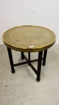 A CIRCULAR BRASS TOP OCCASIONAL TABLE WITH IRANIAN DESIGN ON FOLDING OAK BASE DIA. 59CM.