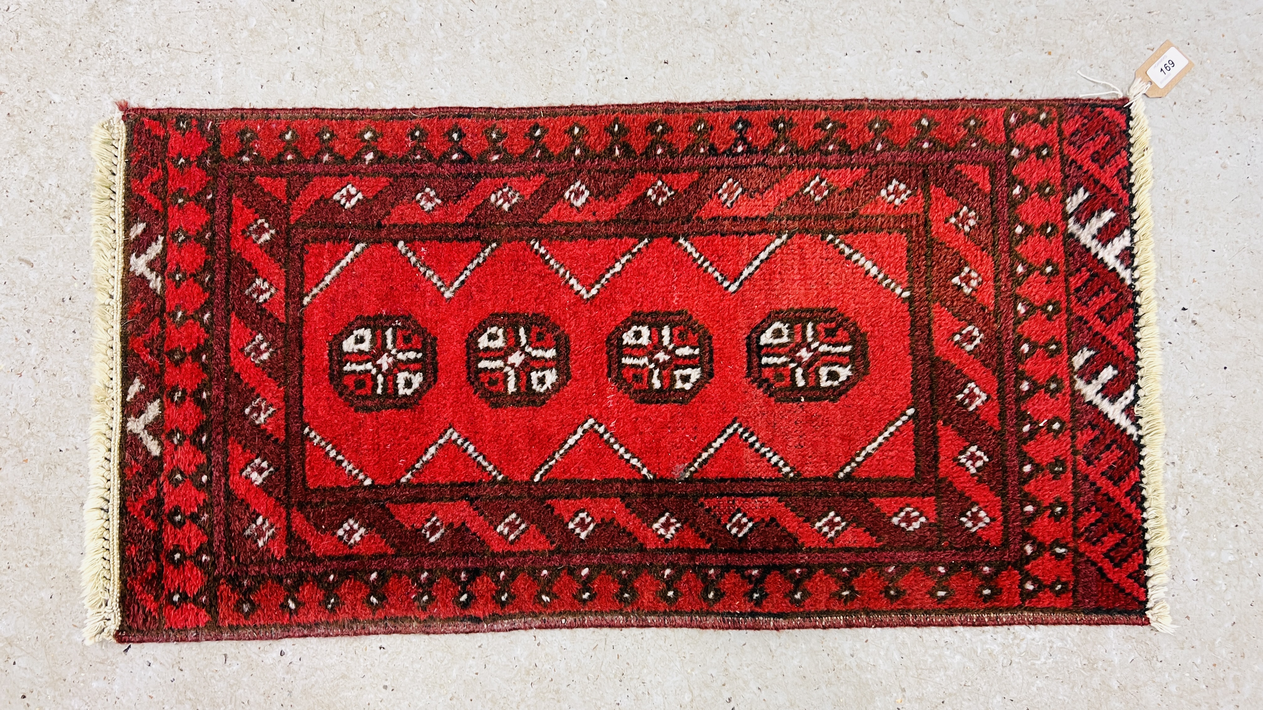 A SMALL RED PATTERNED EASTERN RUG 94CM. X 48CM.