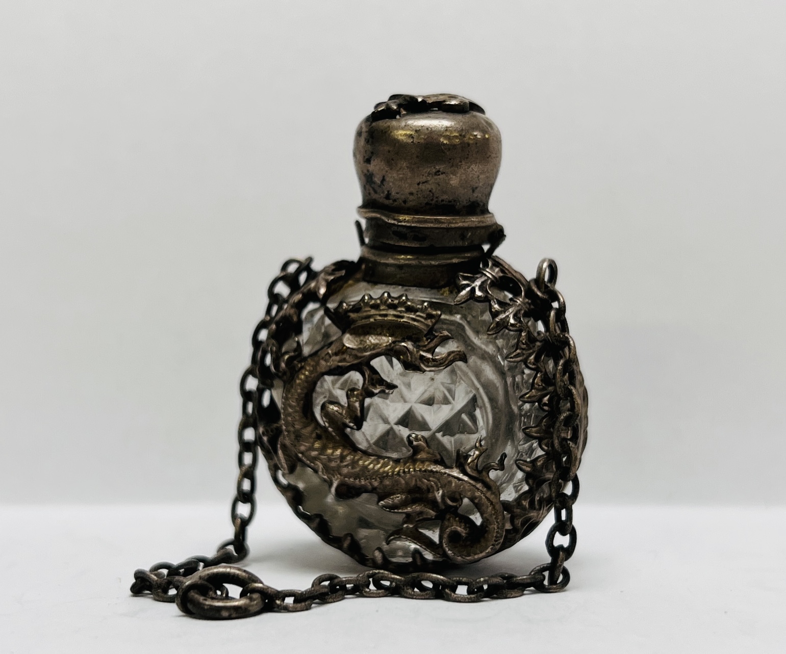 A MINIATURE ANTIQUE CUT GLASS SCENT BOTTLE ENCASED IN AN ORIENTAL WHITE METAL HOLDER