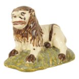 AN EARLY 19TH CENTURY STAFFORDSHIRE SCULPTURE OF A RECUMBENT LION