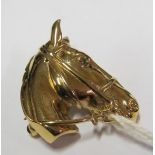 A gold coloured horses head brooch with green stone eye