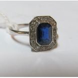 An Art Deco style sapphire and diamond ring central emerald cut sapphire surrounded by diamonds on