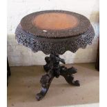 An Indian hardwood circular tip-up action table with carved shaped frieze on tripod and carved