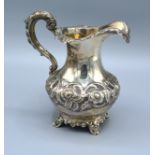 A Victorian Silver Jug of bulbous form with embossed floral decoration upon four scroll feet and