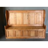 A Large Pine Settle, the panelled back above a lift up seat with shaped ends raised upon a plinth