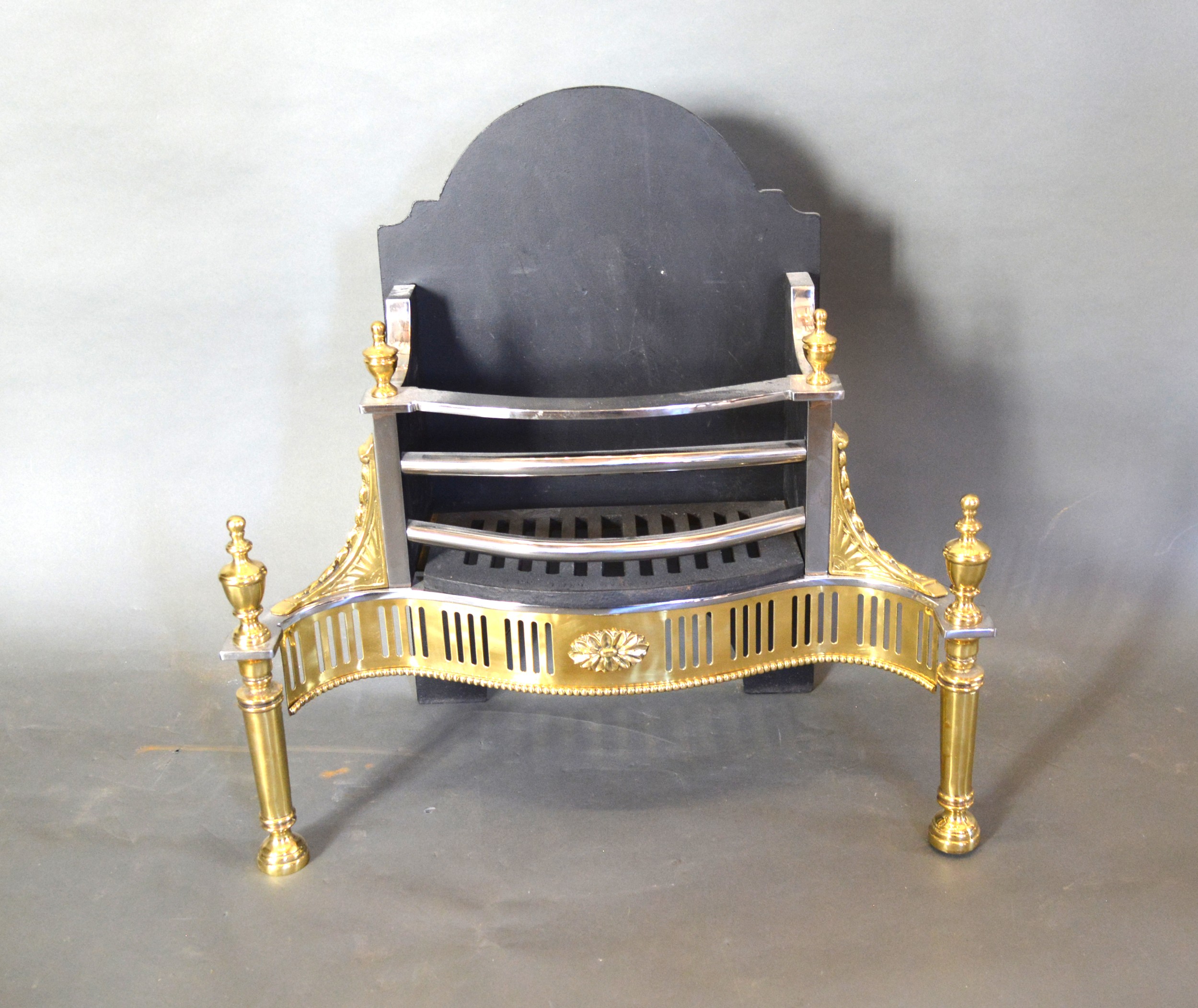 A Regency Style Iron Steel and Brass Fire Basket of shaped form with brass finials 61 cms wide, 29