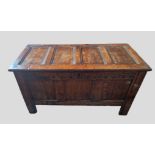 An 18th Century Oak Coffer, the hinged top above a carved frieze and three panel front flanked by