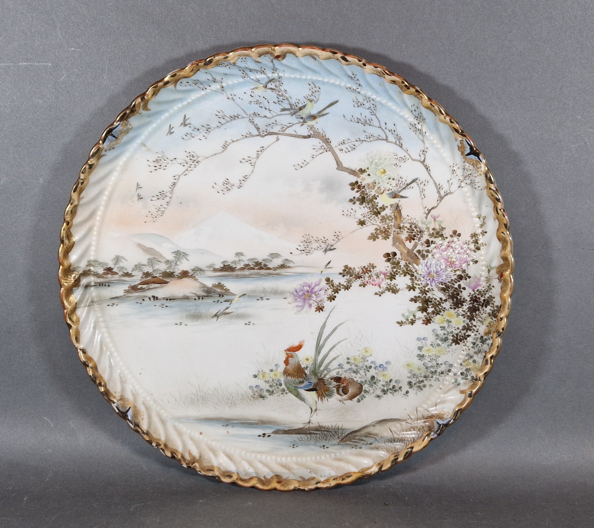 A Japanese porcelain large dish decorated with a cockerall amongst foliage with mountains in the