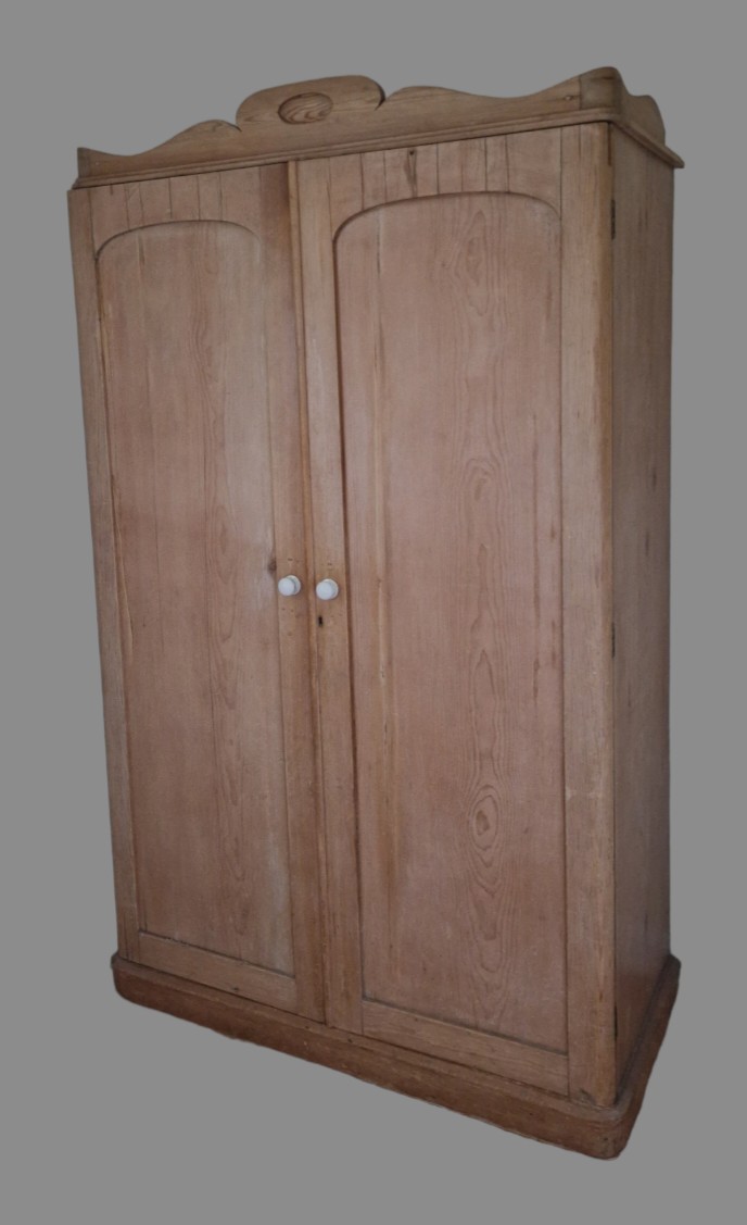 A pine wardrobe, the moulded cornice above two panel doors enclosing hanging space and drawers