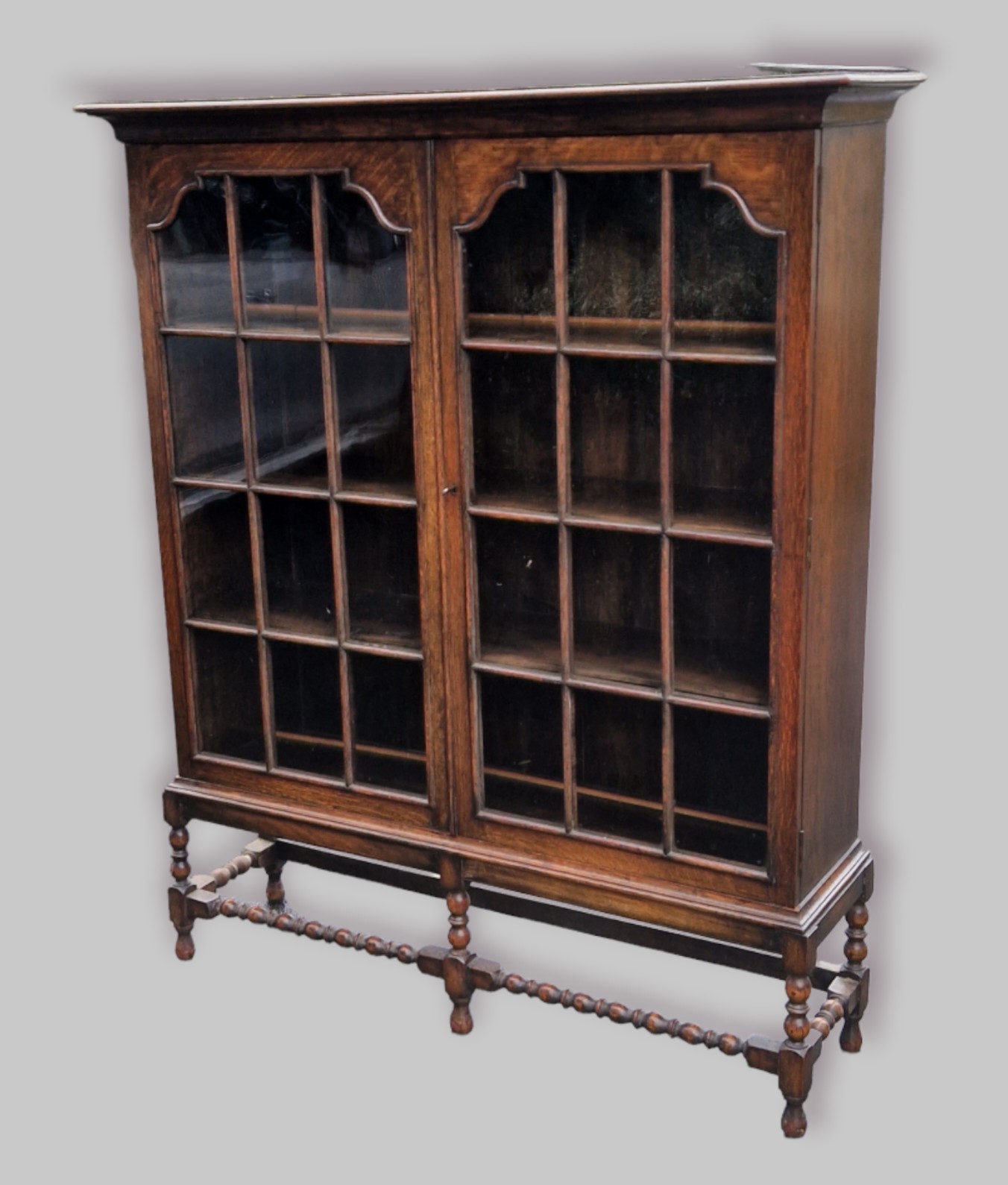 An early 20th Century oak display cabinet, the moulded top above two glazed doors enclosing