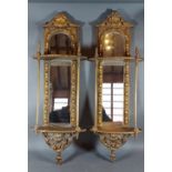 A pair of gilded wall brackets, each with a mirrored back of arched form, 70cms tall