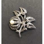 A Silver coloured brooch with white stones and pearl. Floral design brooch featuring a cultured