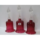 ANTIQUE GLASS, 3 cranberry glass table bells with ribbed glass handles and opaque glass rims, 32cm