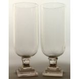 A GOOD PAIR OF GLASS STORM LAMPS on square stepped bases, 16ins high.