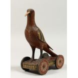 A PAINTED WOODEN FOLK ART BIRD, the base with four wheels. 8ins high.