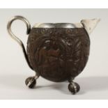 A SILVER CARVED COCONUT SKULL JUG with carved panels on claw and ball feet. 3.5ins diameter.