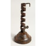 AN EARLY METAL CANDLESTICK on a circular wooden base. 8ins high.