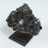 A BLACK CRYSTALINE SPECIMEN on a stand.