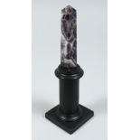 AN AMETHYST OBELISK on a wooden stand 4ins high.