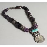 AN ISLAMIC AMETHYST, TURQUOISE AND SILVER HEAD NECKLACE by Arlene Coyne, set with a coin.