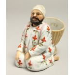 A SMALL ARAB PORCELAIN FIGURE of a man carrying a basket, with a nodding head. 3.5ins high.