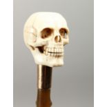 A RUSTIC RHINO PART RIDING CROP with carved ivory skull handle. 10ins long.
