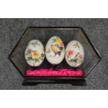 Three Chinese painted eggs in a glass case.