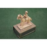 A carved figure on horseback mounted on a silver matchbox case.