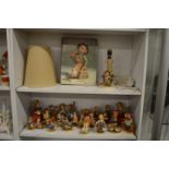 A large collection of Hummel figures, a table lamp and book.