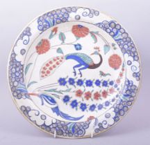 A TURKISH OTTOMAN IZNIK POTTERY DISH, the centre painted with a peacock and flora, 31cm diameter.