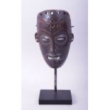 A SMALL CARVED WOOD AFRICAN MASK, raised on a wooden stand, mask 18cm x 11.5cm.