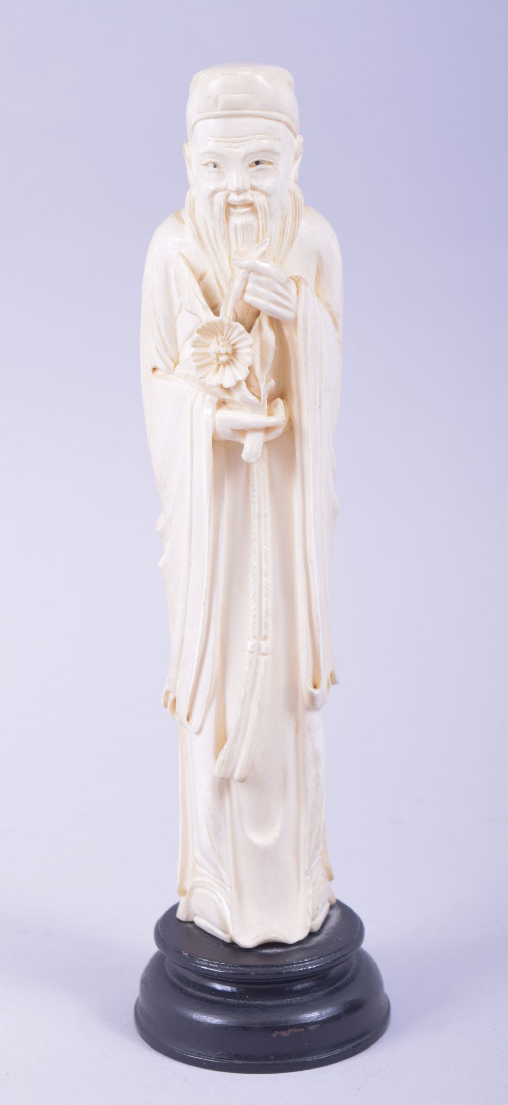 A CHINESE CARVED IVORY FIGURE OF A SAGE holding a flower, mounted to a hardwood base, 23cm high.