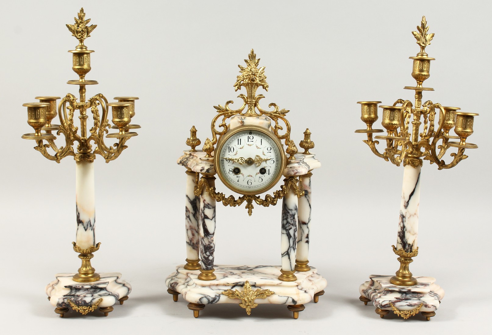 A LOUIS XVI DESIGN VEINED MARBLE AND ORMOLU CLOCK GARNITURE, the side pieces with four scrolling