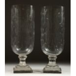 A PAIR OF GLASS STORM LAMPS on stepped square bases. 16ins high.