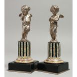 A SUPERB PAIR OF 19TH CENTURY SILVER AND ENAMEL CUPIDS on columns and square bases. 16cm high.