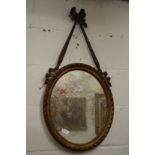 A decorative oval mirror with ribbon cresting.