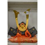 A cast metal model of a Samurai helmet on a gilt embroidered cushion.