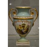 A porcelain twin handled pedestal vase painted with a river landscape.