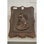 A relief cast bronze plaque of Dickens on an oak panel.