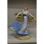 A continental porcelain figure of a lady with a basket of flowers in each hand.