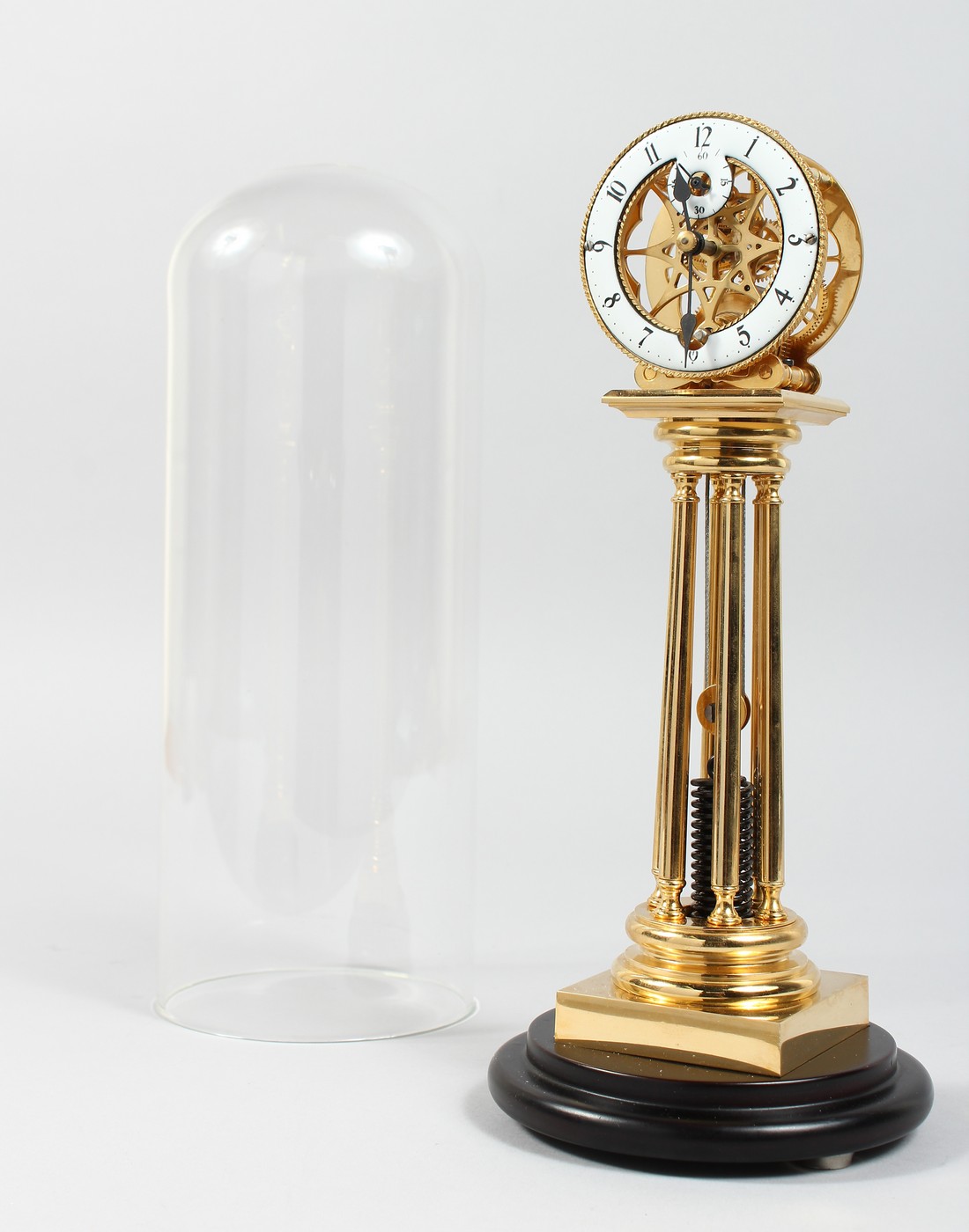 AN UNUSUAL BRASS COLUMN CLOCK with enamel dial, large spring driven movement, under a glass dome.