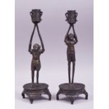 A PAIR OF JAPANESE BRONZE FIGURAL CANDLESTICKS, each formed as a male figure upon a base with arms