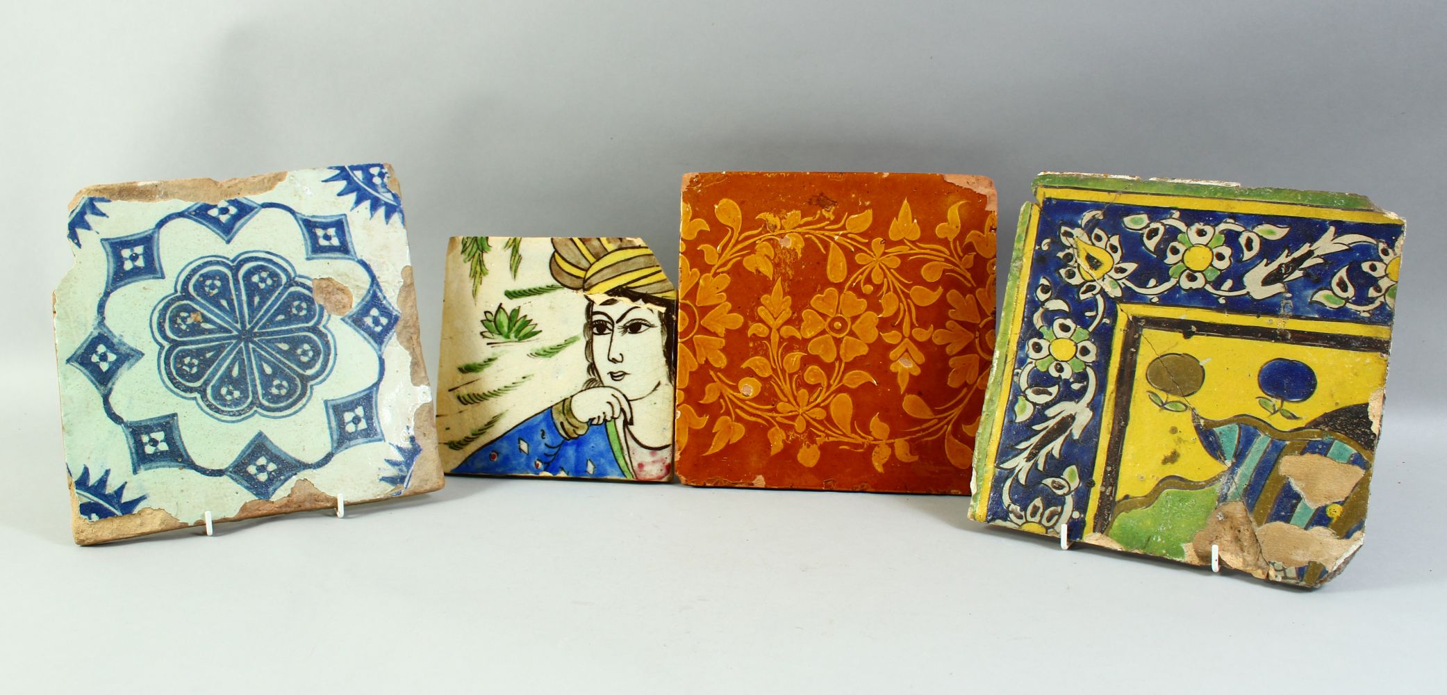 FOUR ISLAMIC GLAZED POTTERY TILES, three with foliate decoration and one with a section of a figure,