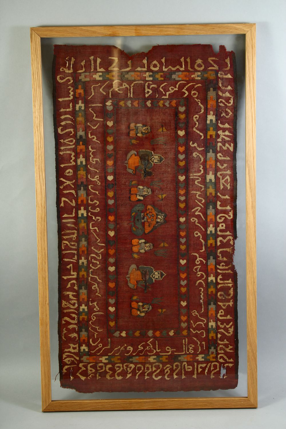 AN ISLAMIC TEXTILE FRAGMENT, the textile embroidered with seated figures and with bands of script,